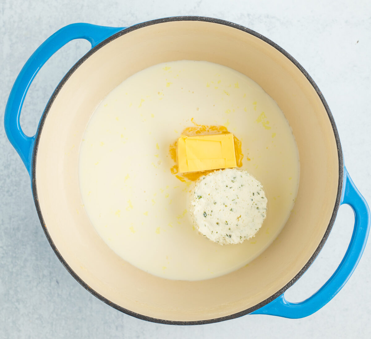 butter, cream, and herbed cheese in a blue Dutch oven.