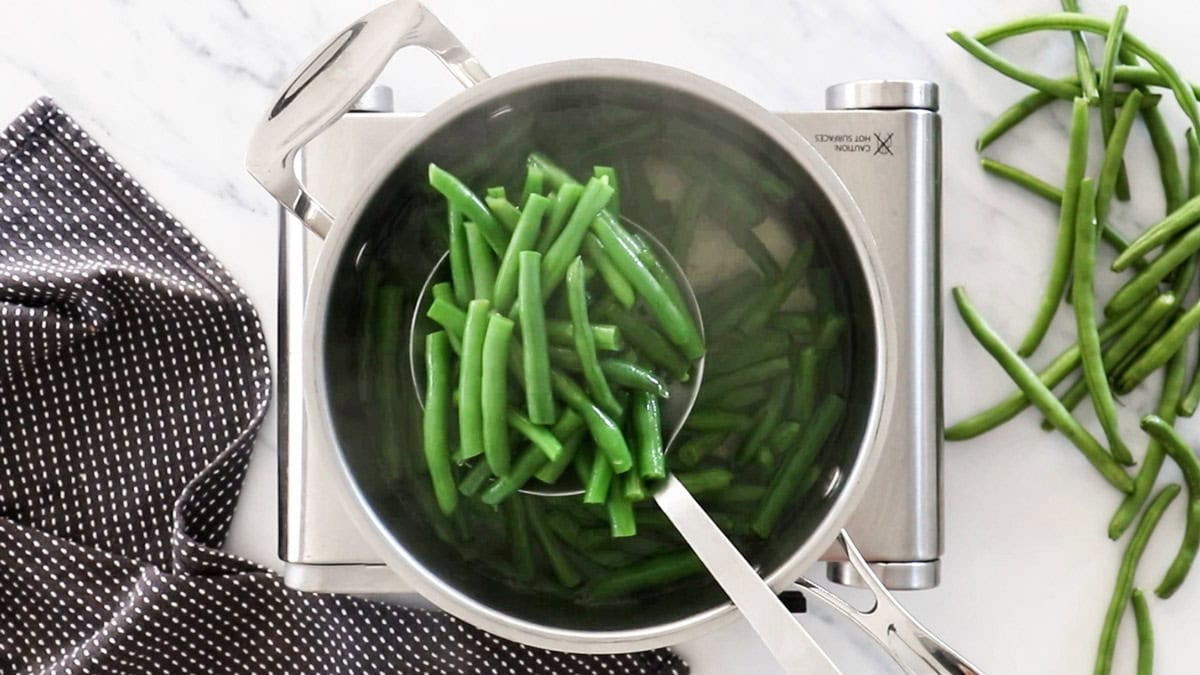 a spoon holding green beans over a saucepan of water.