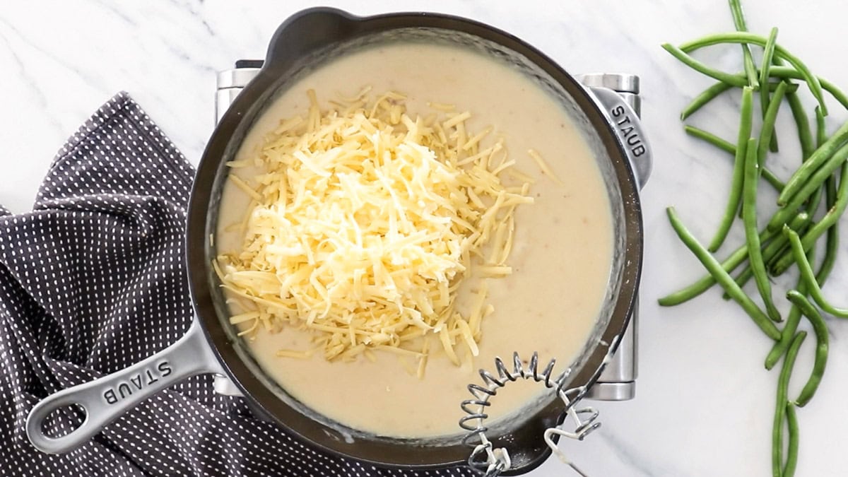 cheese in a sauce in a skillet with a whisk.