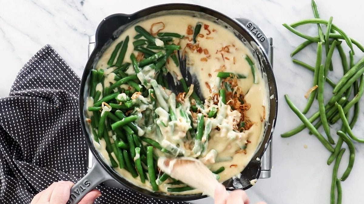 green beans and fried shallots being mixed into a cheese sauce.