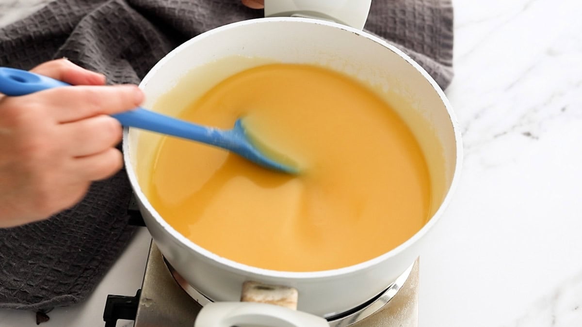 a blue spoon stirring a milk-based sauce in a white saucepan.