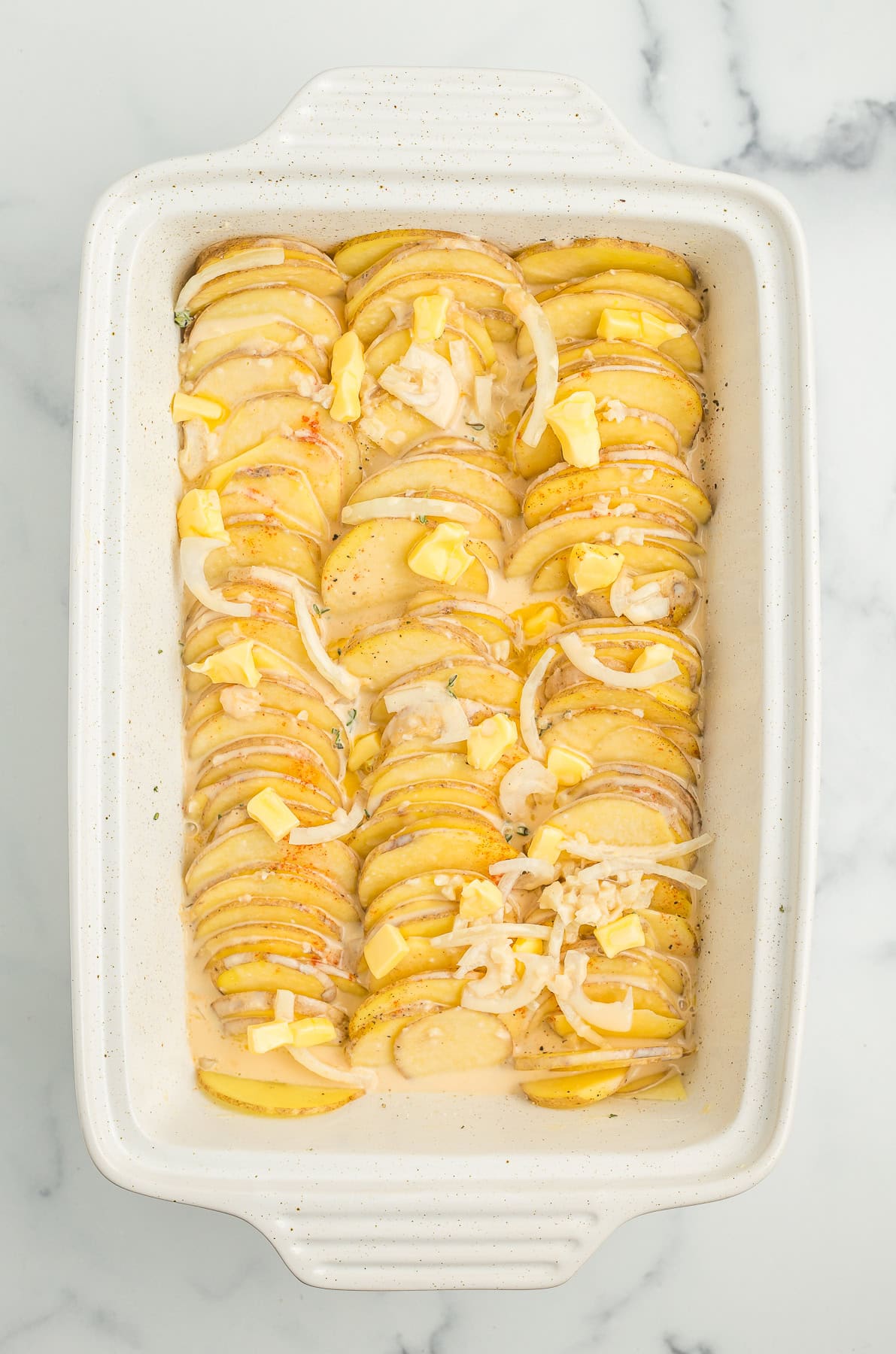 sliced Yukon golds in a sauce in a white casserole dish.
