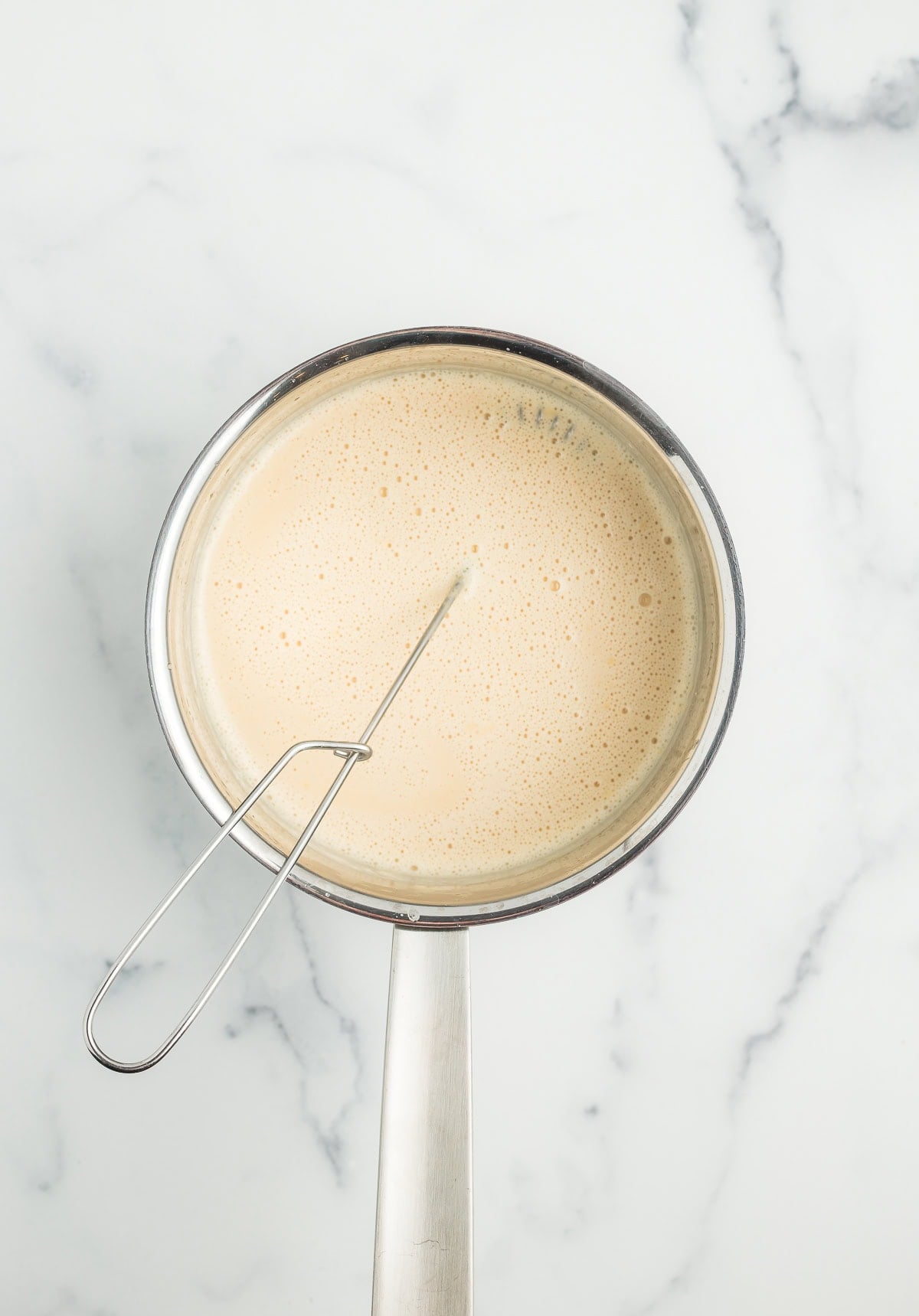 a whisk in a saucepan full of milk.