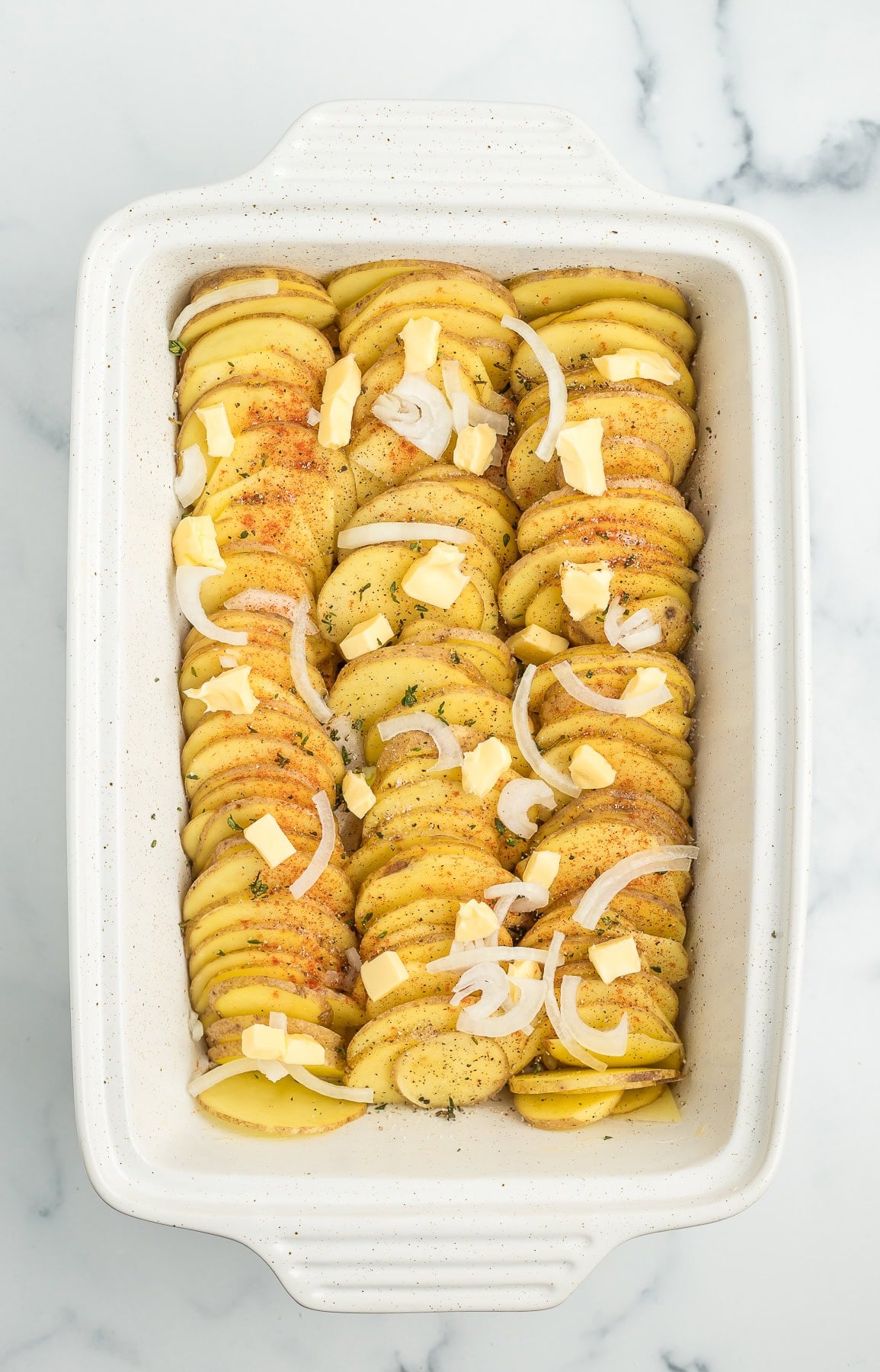 sliced Yukon golds, onions, and butter in a white baking dish.