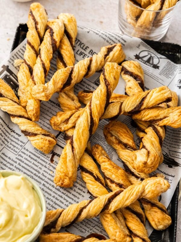 puff pastry cinnamon twists on a piece of newspaper with a small bowl of cream cheese dip.