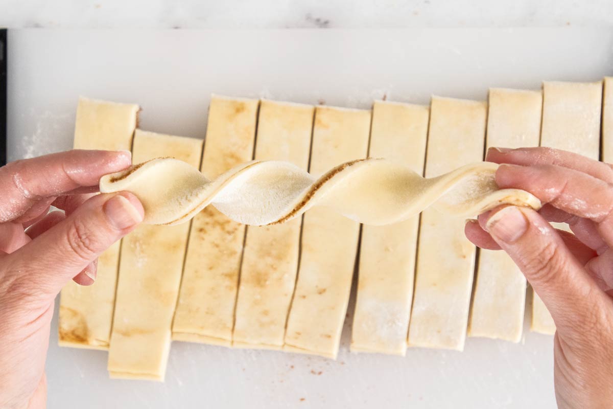 a hand holding a piece of unbaked dough showing how to twist it.