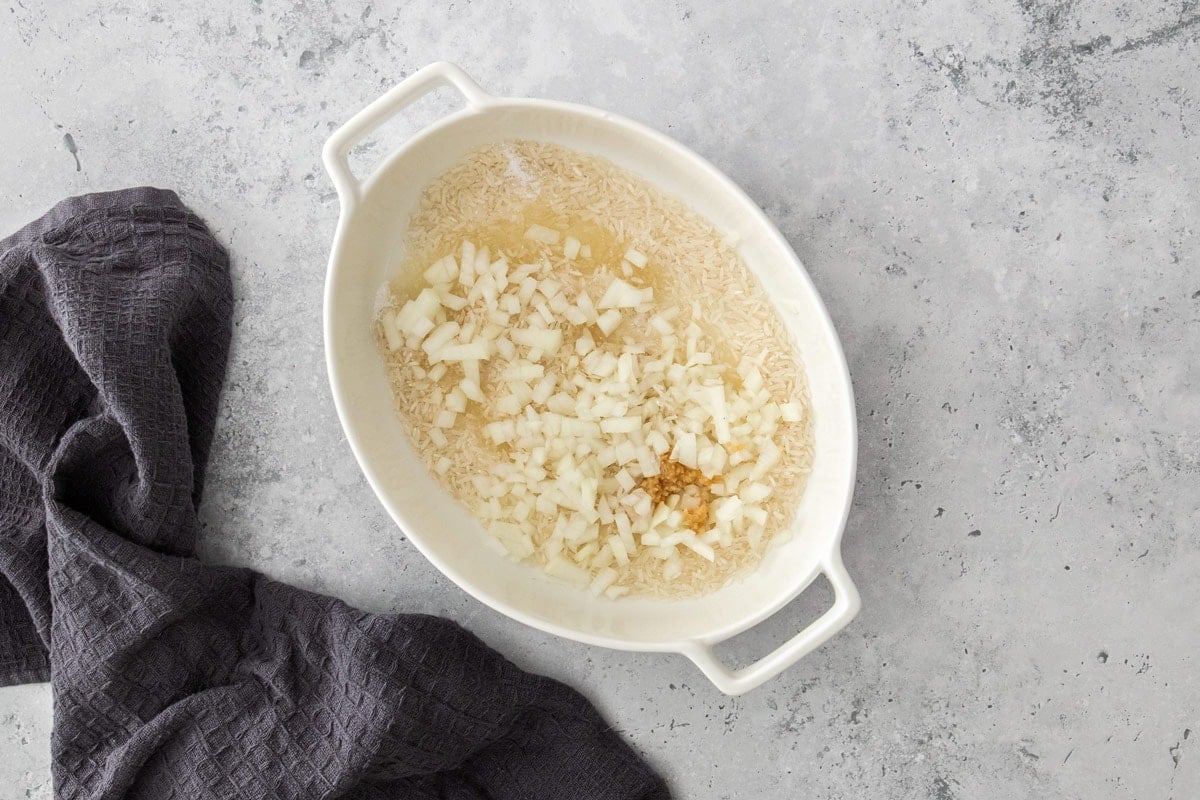 chopped onions, garlic, and rice in a white baking dish.