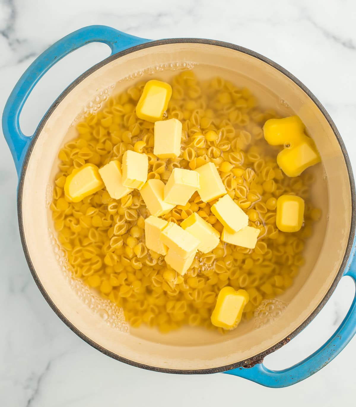 butter, water, and noodles in a blue Dutch oven.