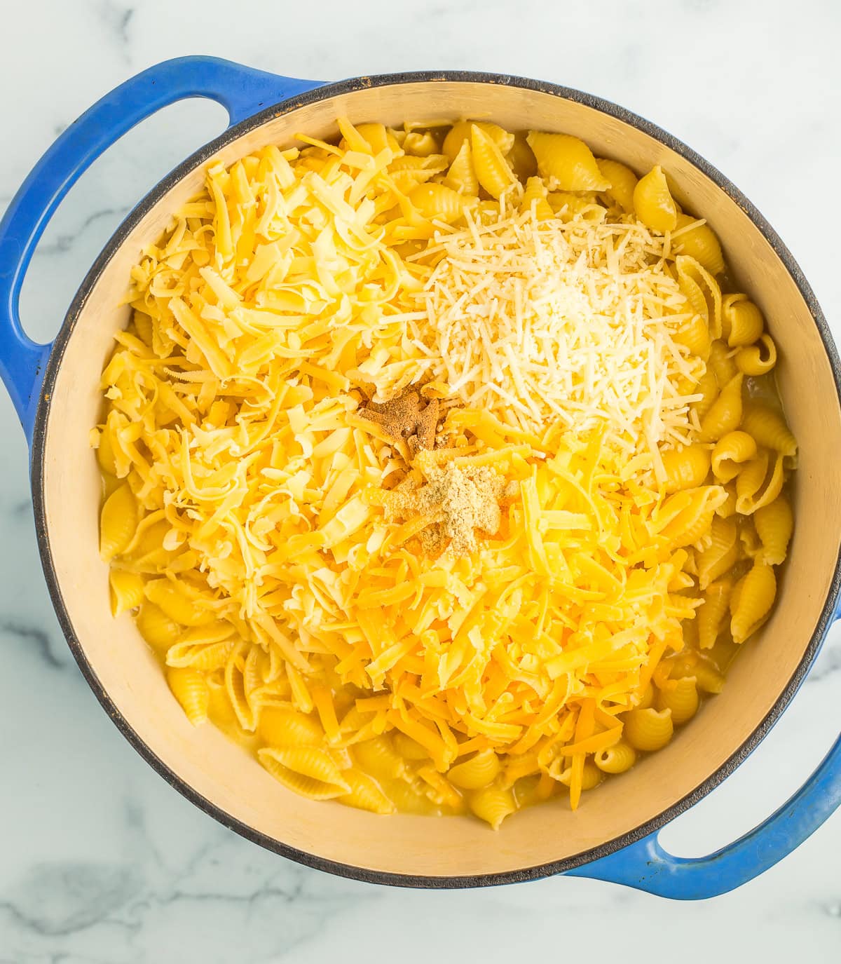 shredded cheese and shells in a blue Dutch oven.