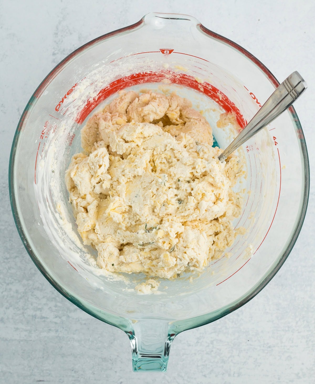 unbaked dough with herbs in it in a glass mixing bowl with a spoon.