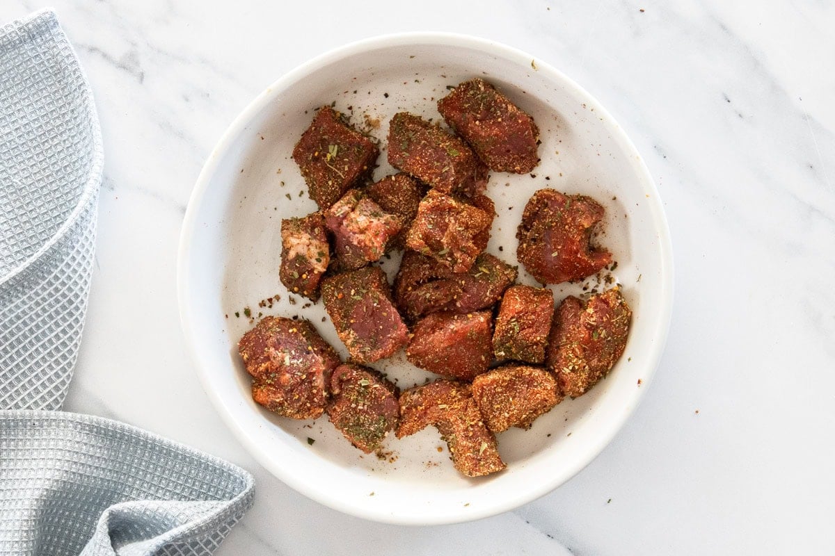 cubes of top sirloin tossed in herbs in a white bowl.