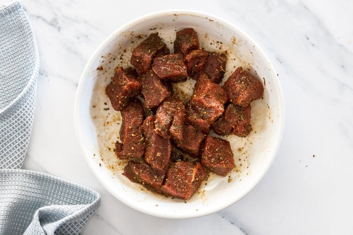 cubes of top sirloin tossed in olive oil in a white bowl.