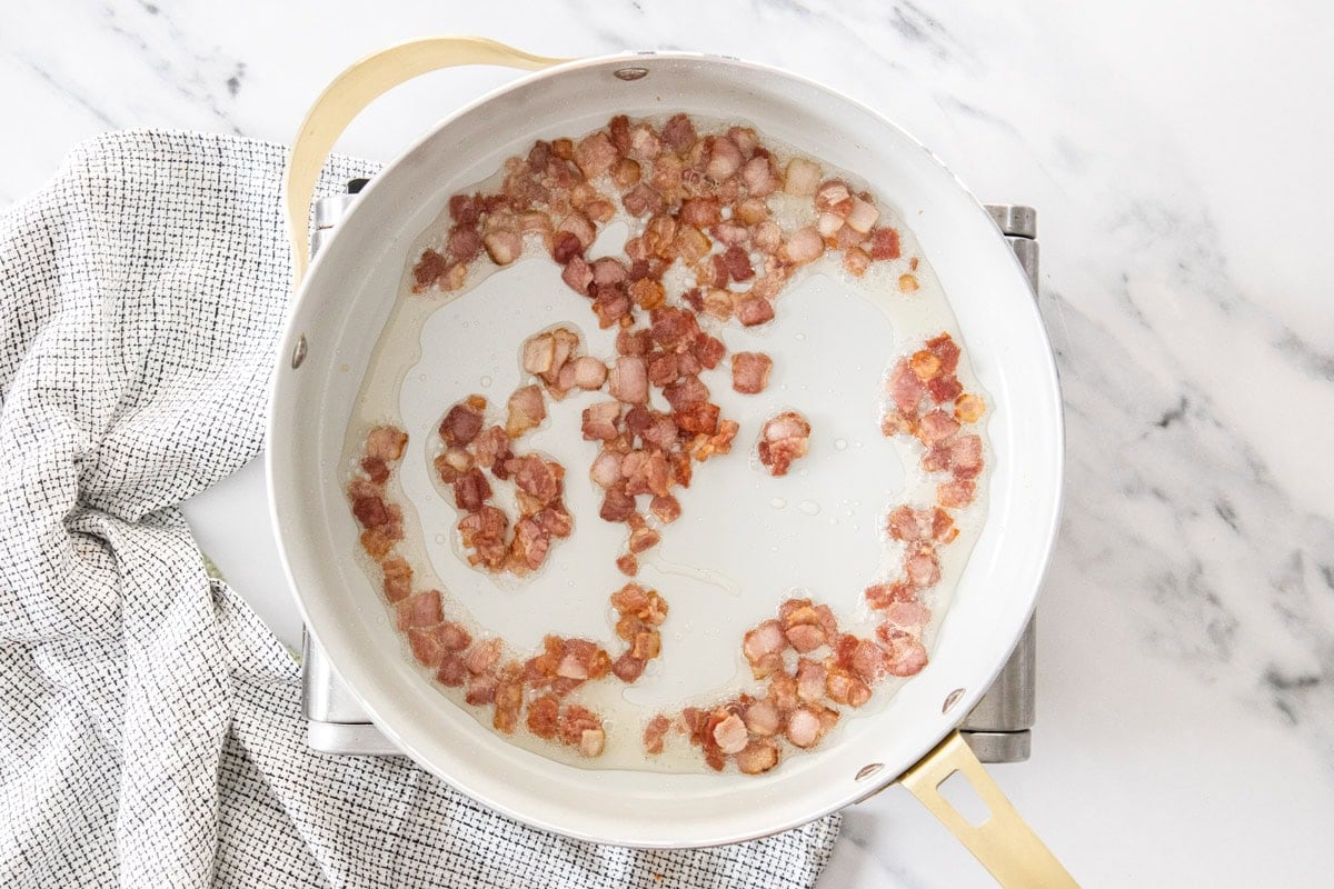 pieces of bacon cooking in a skillet.