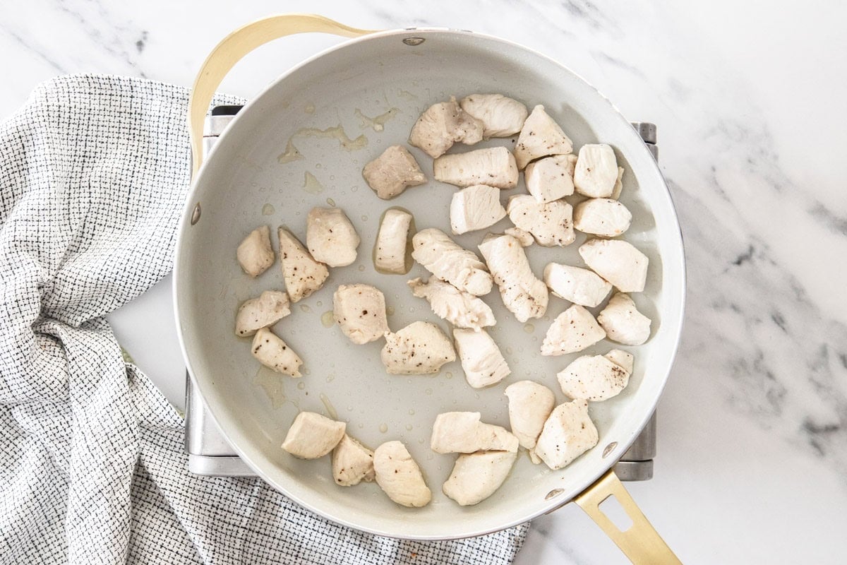 cubes of chicken cooking in a skillet.