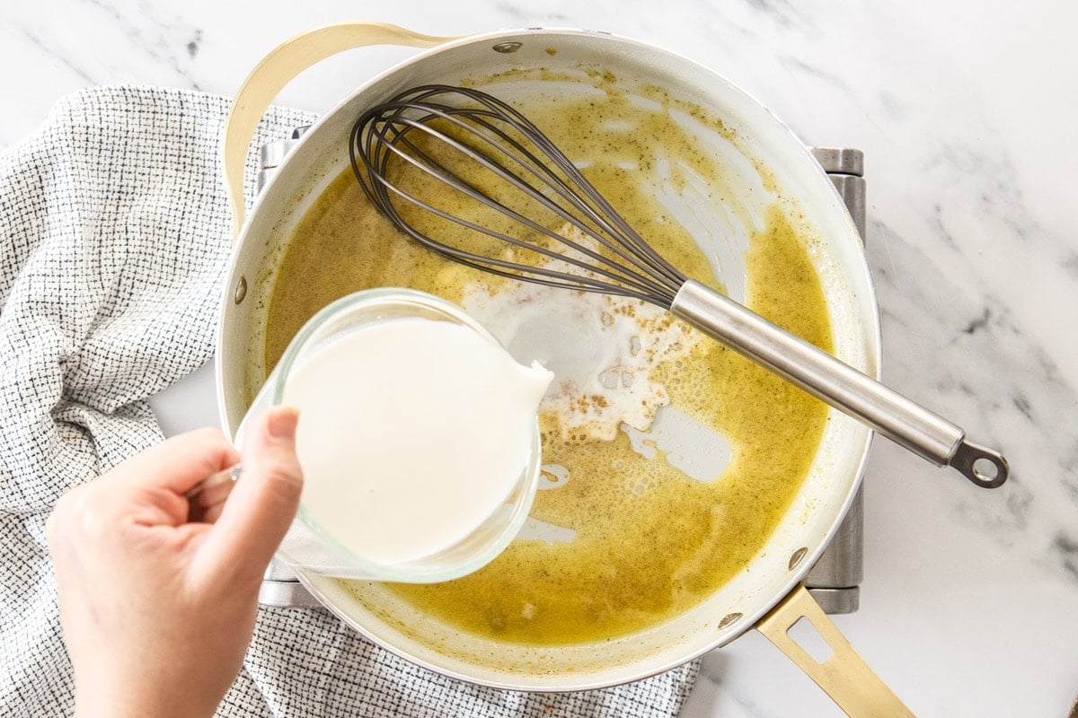 milk in a measuring cup being poured into a skillet.