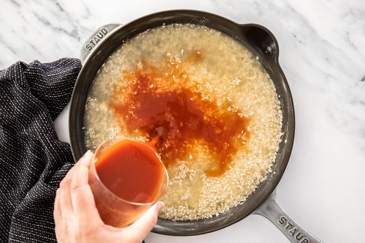 a glass of vegetable juice being poured into a skillet of rice and broth.