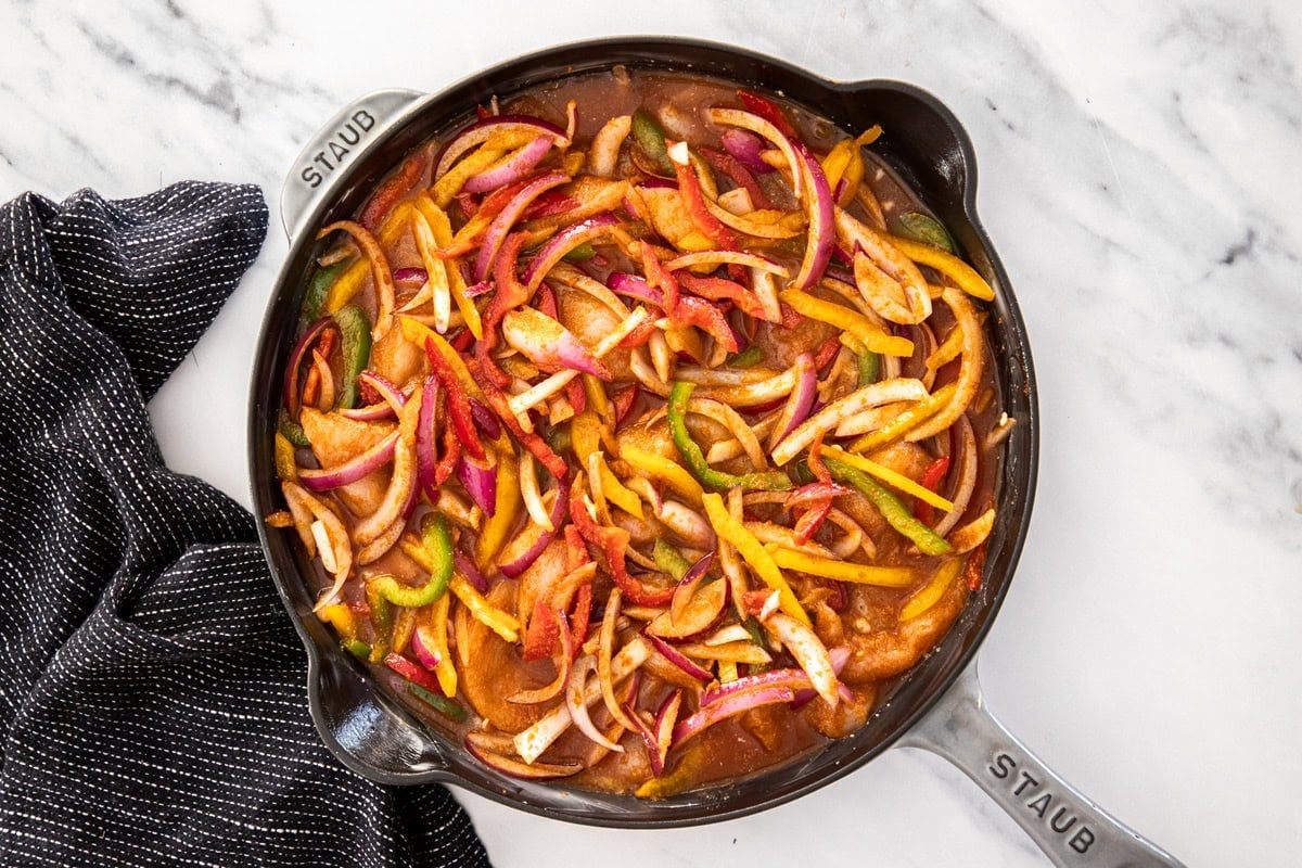 uncooked sliced peppers and onions on top of other ingredients in a cast iron skillet.
