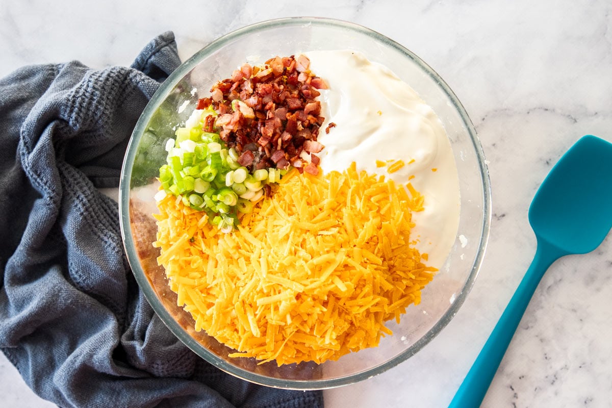 shredded cheese, green onions, bacon, and sour cream in a glass bowl.