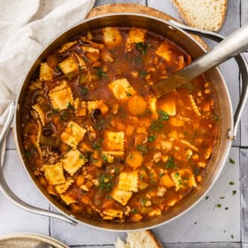 a stainless pot filled with cheese ravioli and sausage soup and a metal ladle.