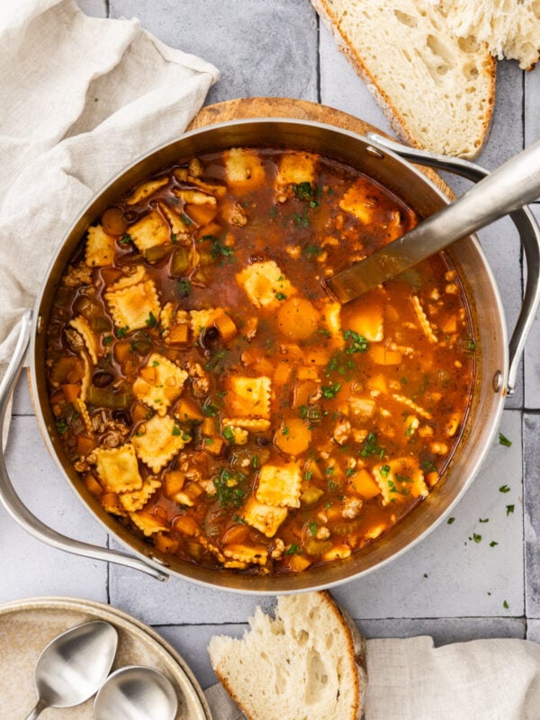 a stainless pot filled with cheese ravioli and sausage soup and a metal ladle.