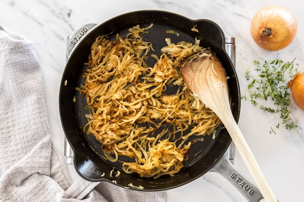 sliced onions being caramelized in a cast iron skillet with a wooden spoon.
