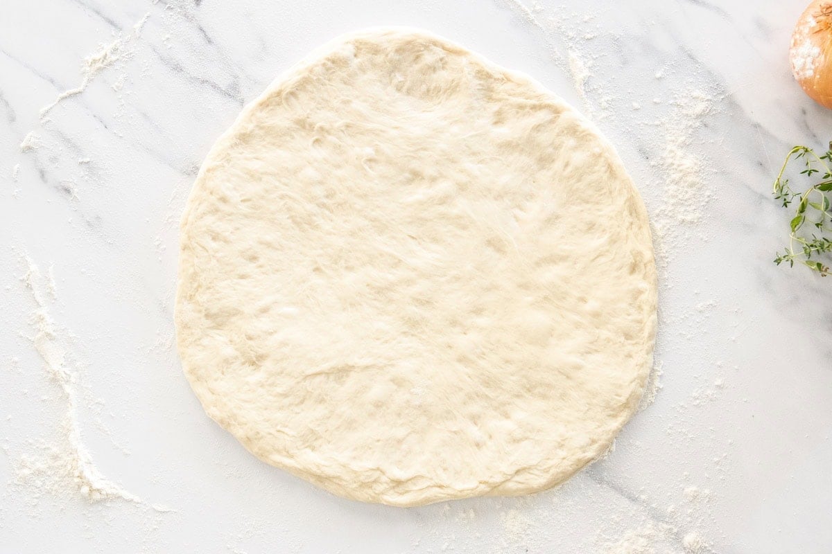 pizza dough patted out on a marbled board.