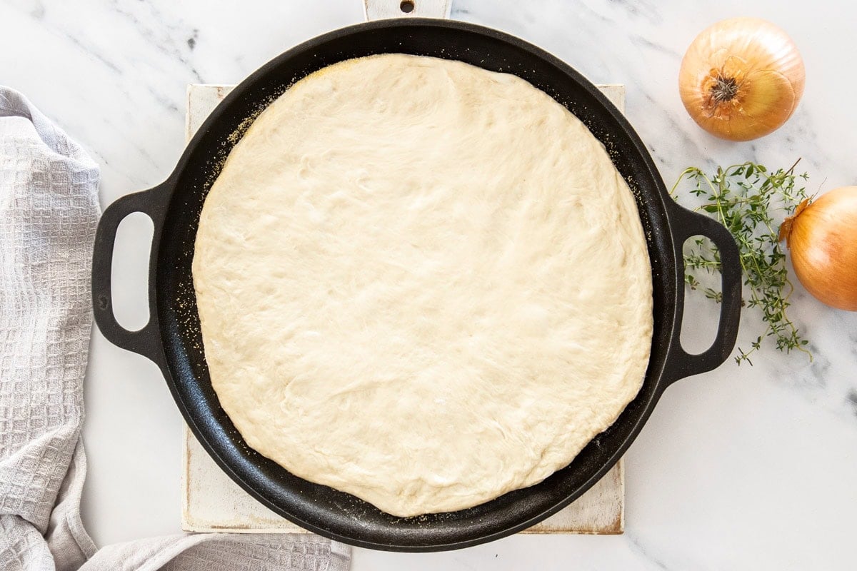 pizza dough patted out on a cast iron pizza pan.