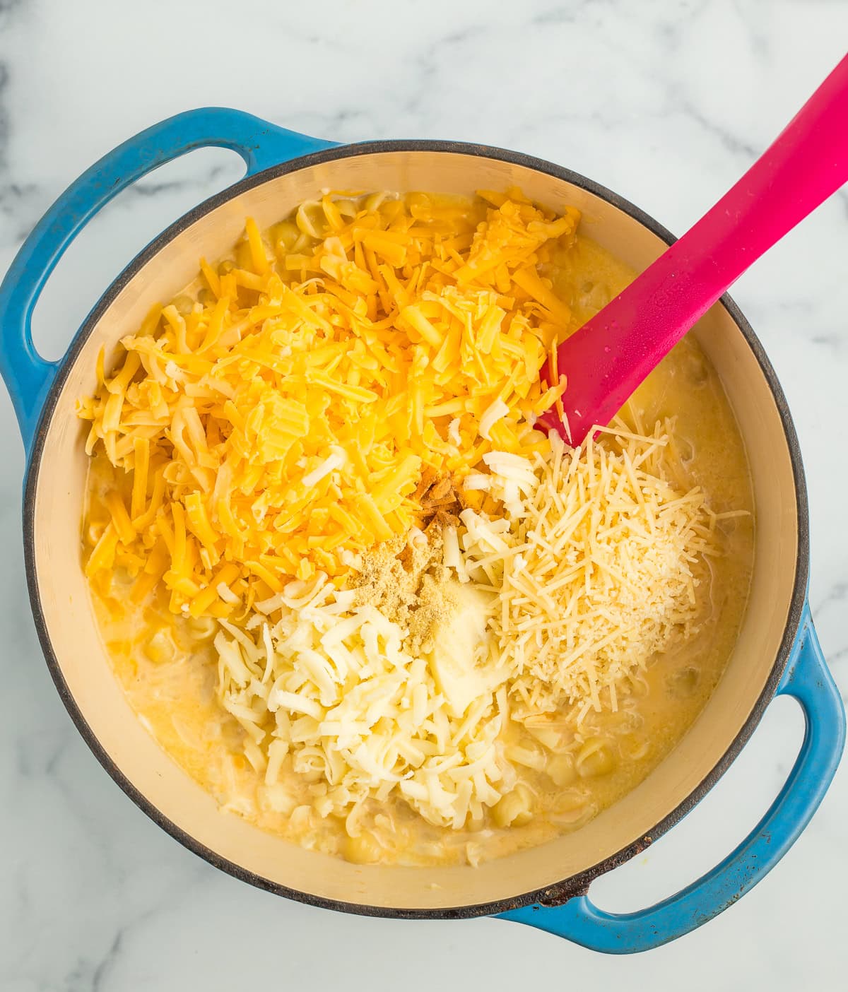shredded cheese and noodles in a blue Dutch oven.