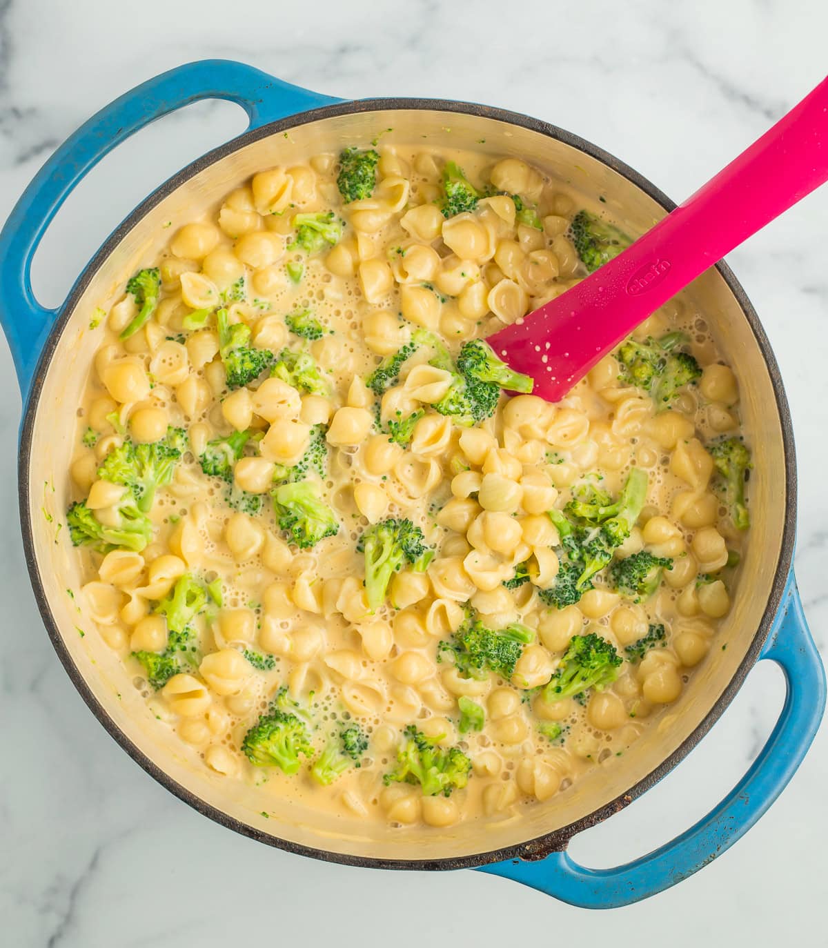 pieces of broccoli stirred into a blue Dutch oven.