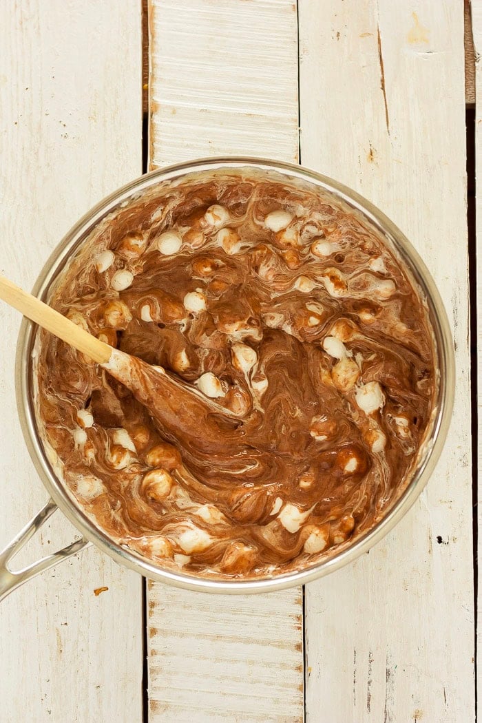 a wooden spoon mixing marshmallows into a chocolate mixture.