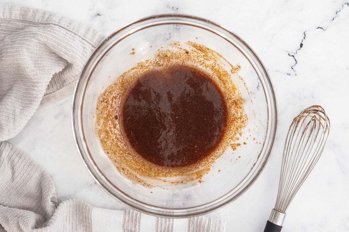 a marinade in a glass bowl with a whisk on the side.