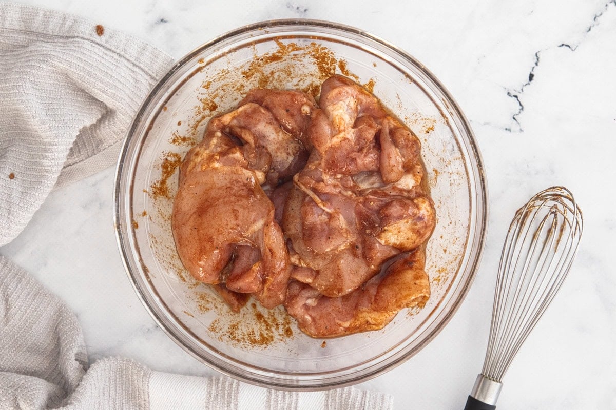 uncooked chicken marinating in a glass bowl.