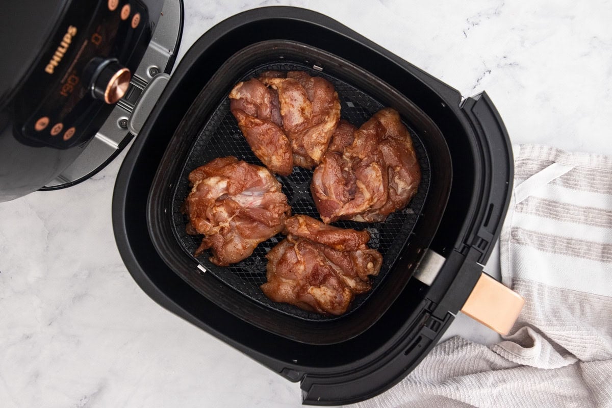 four uncooked chicken thighs in an air fryer basket.