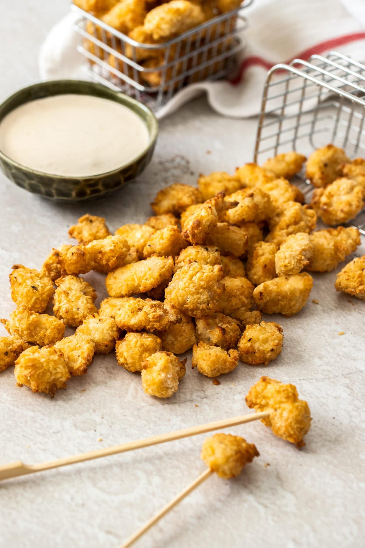 pieces of breaded poultry spilling from a basket with a small bowl of dip.