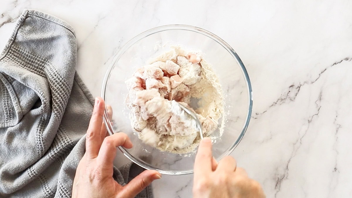 a glass bowl of flour with pieces of chicken being stirred into it.