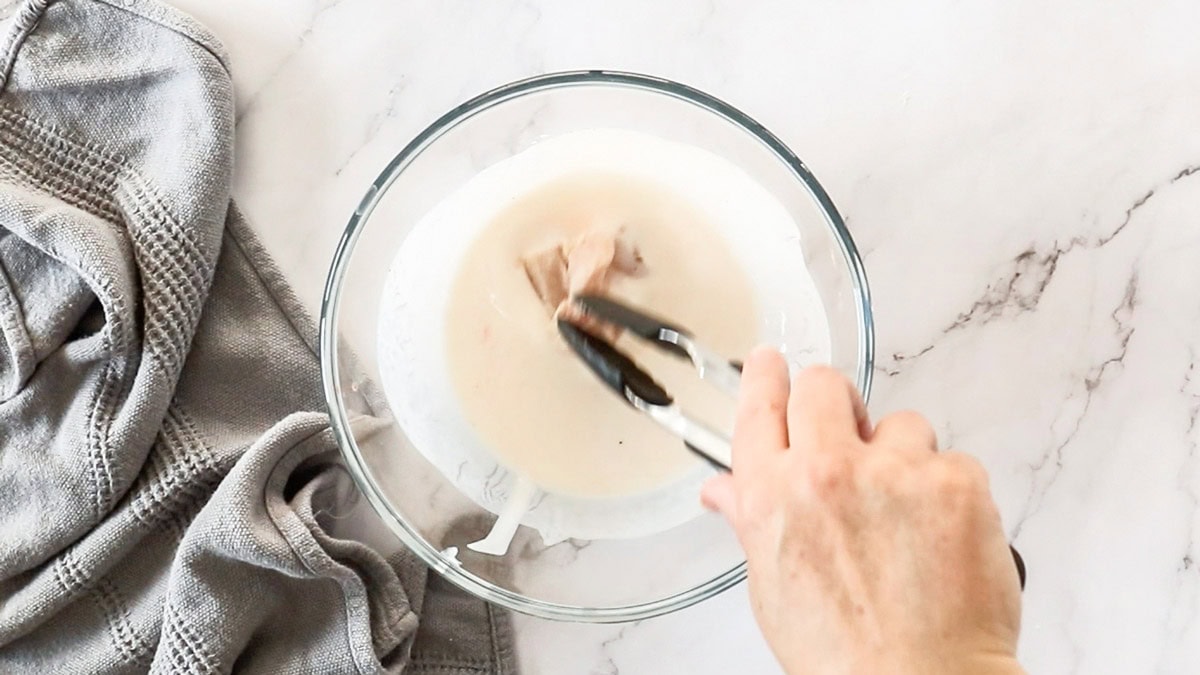 pieces of chicken being dredged through buttermilk.