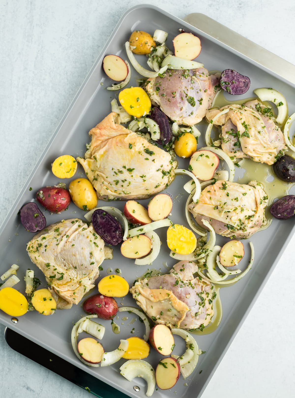 unbaked chicken and potatoes with onions on a baking sheet.