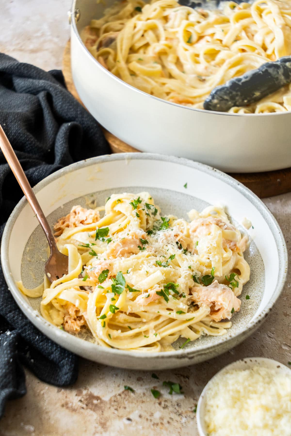a white and grey bowl with pasta topped with parmesan and chopped parsley.