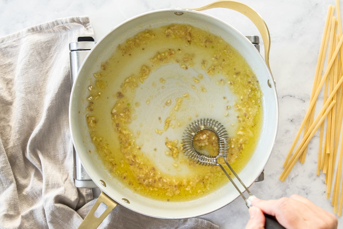 a whisk in a skillet with butter and shallots.