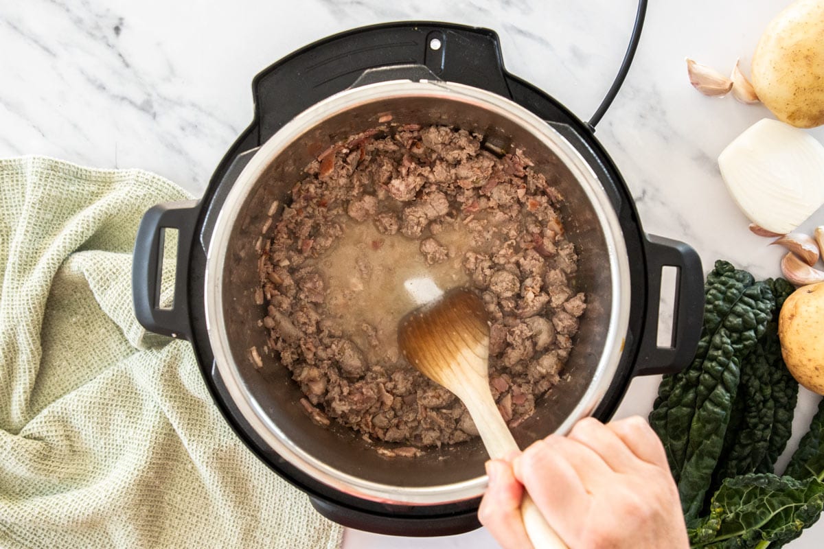 a wooden spoon deglazing the insert of a pressure cooker.