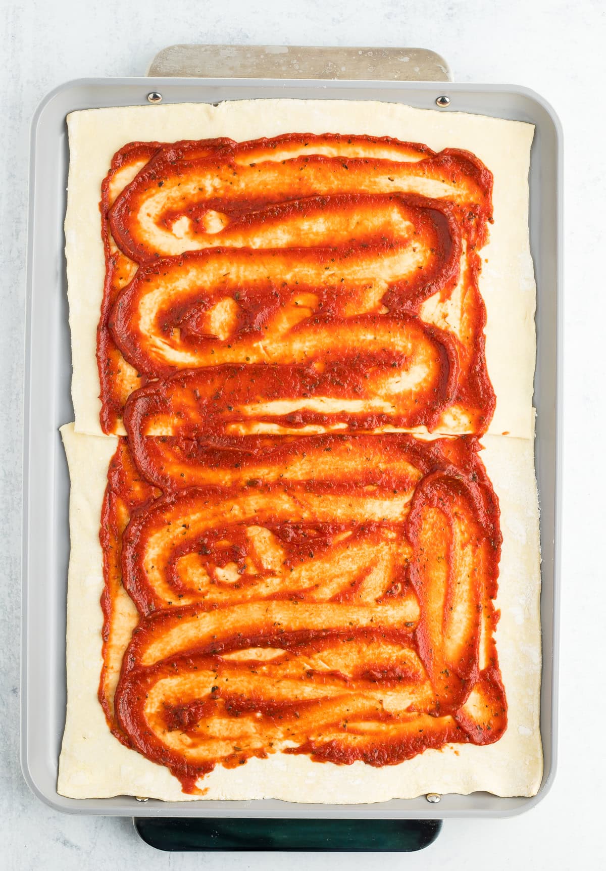 sauce on top of 2 pieces of dough on a baking sheet.