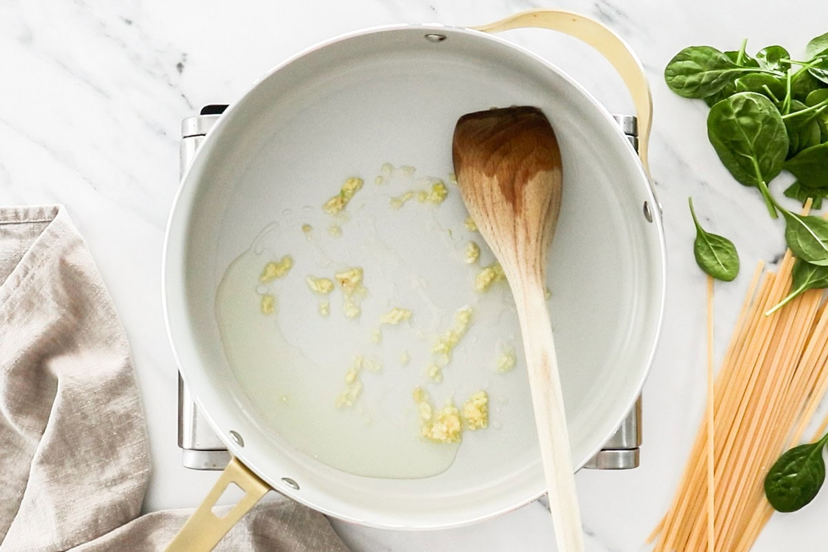 garlic and olive oil in a skillet with a wooden spoon.