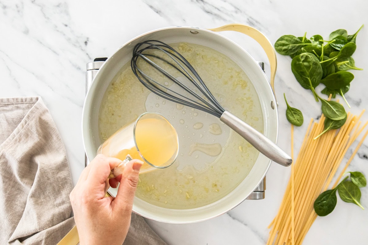 chicken stock being poured into a skillet that has a whisk in it.