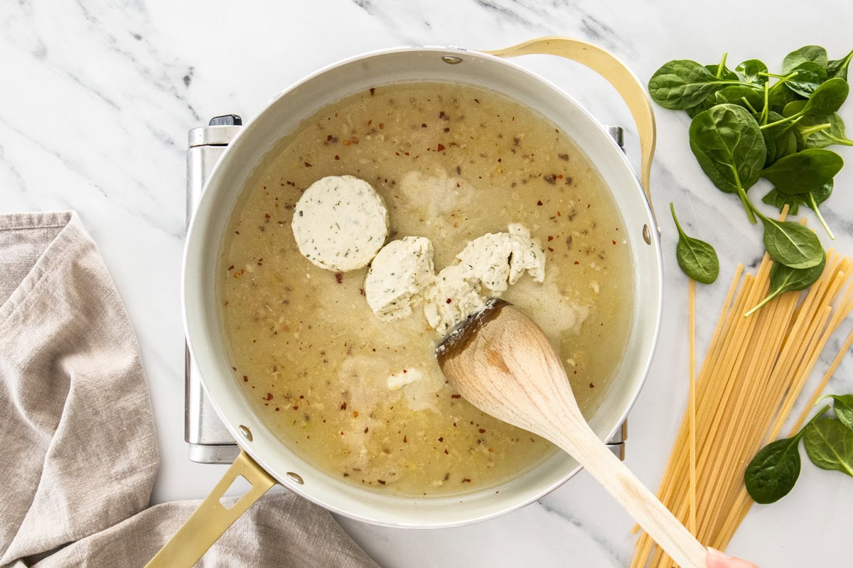 a wooden spoon breaking up cheese into liquid in a skillet.