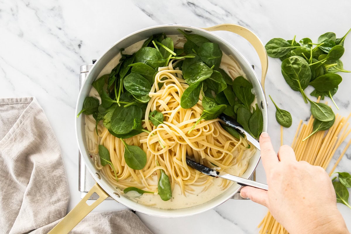 linguine and spinach and a cream sauce in a skillet.
