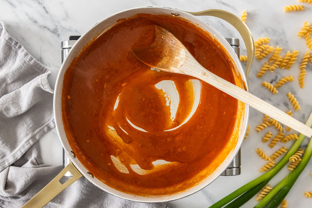 a sauce being cooked in a skillet with a wooden spoon.