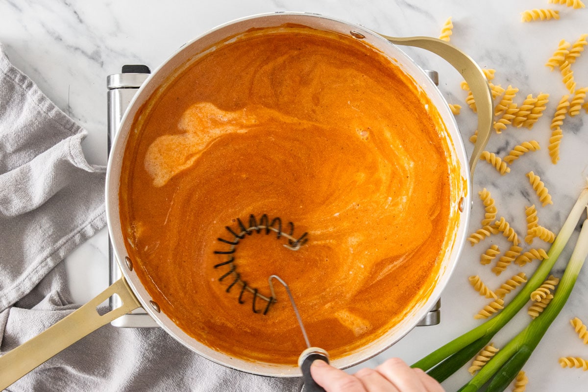 Someone whisking a sauce in a skillet.