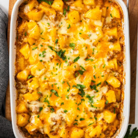 a white baking dish of cheesy hamburger and potato casserole topped with chopped parsley.