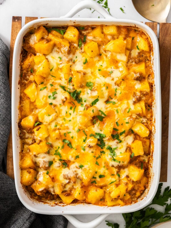 a white baking dish of cheesy hamburger and potato casserole topped with chopped parsley.