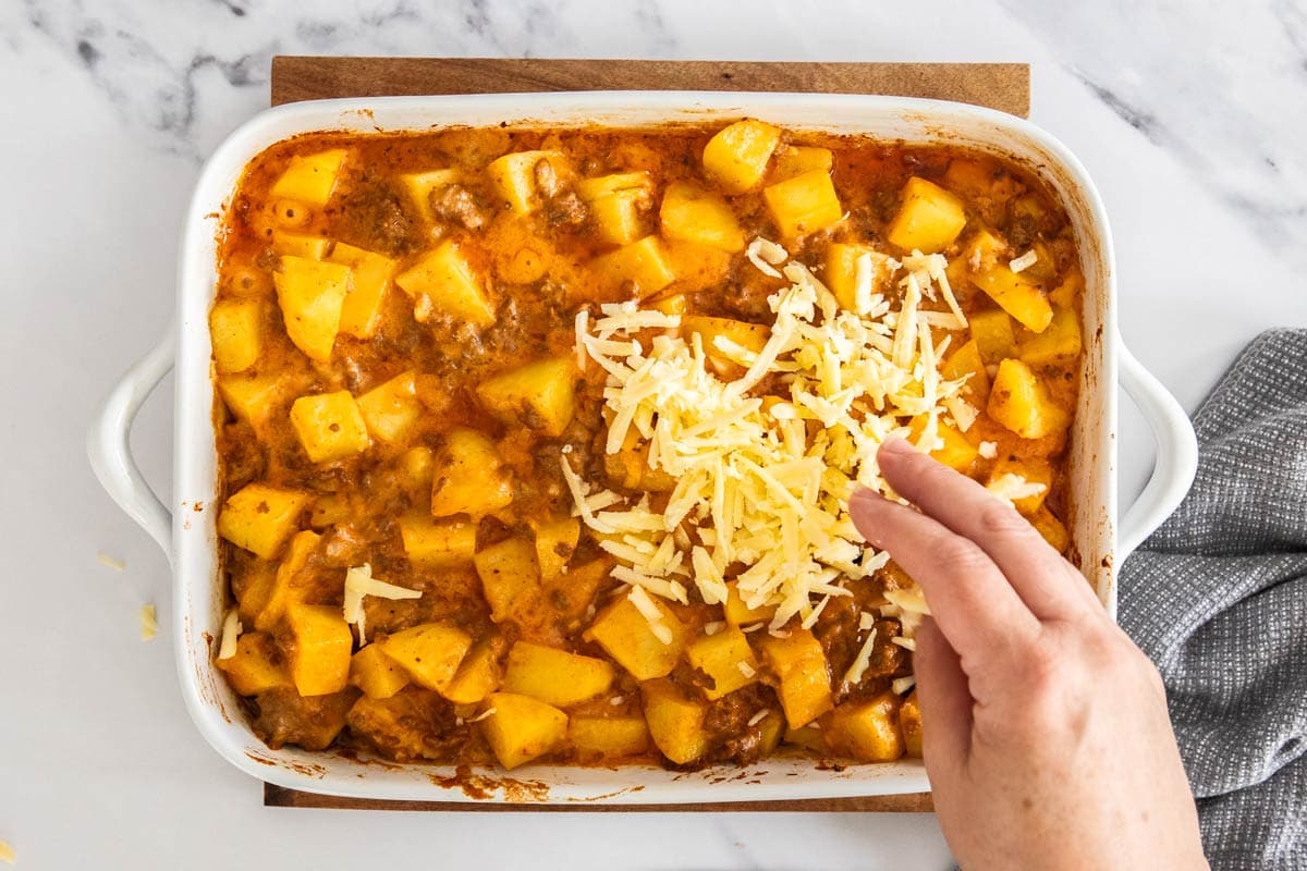 cheese being sprinkled over ingredients in a white baking dish.
